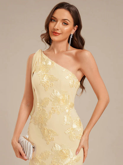 Woman wearing a beige one-shoulder dress with floral embroidery on a beige background