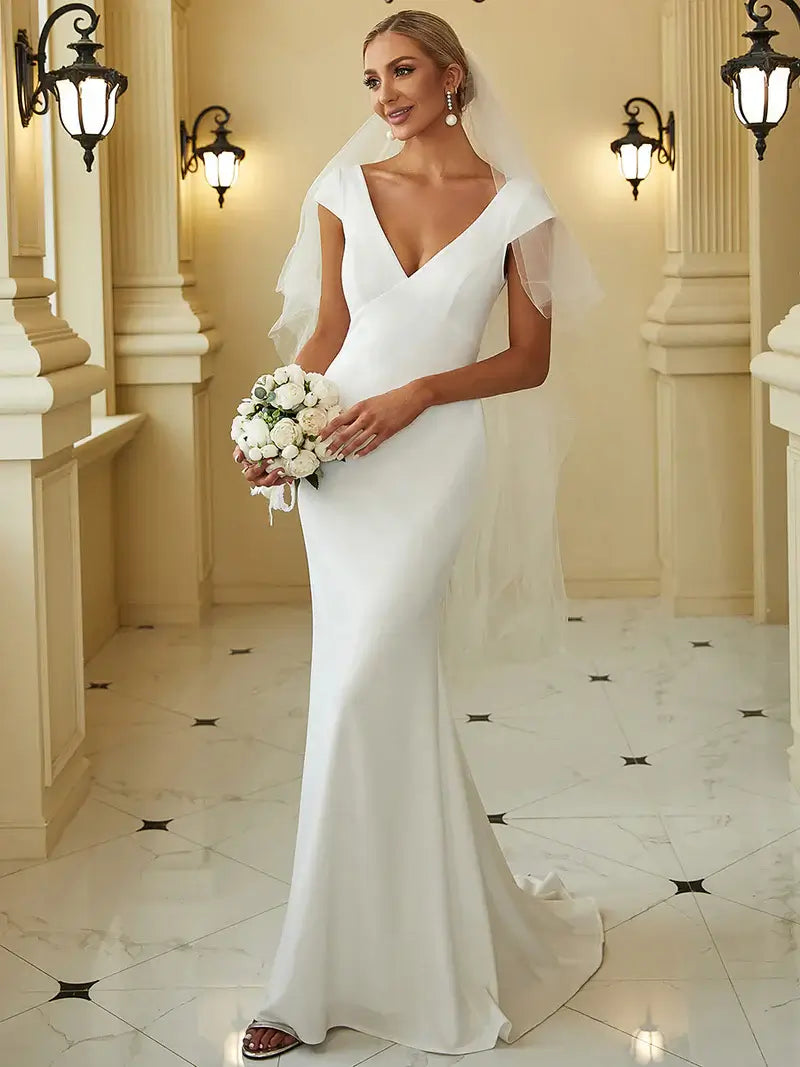 White wedding dress with deep V-neckline, backless design, fishtail silhouette, and sheer cover sleeves